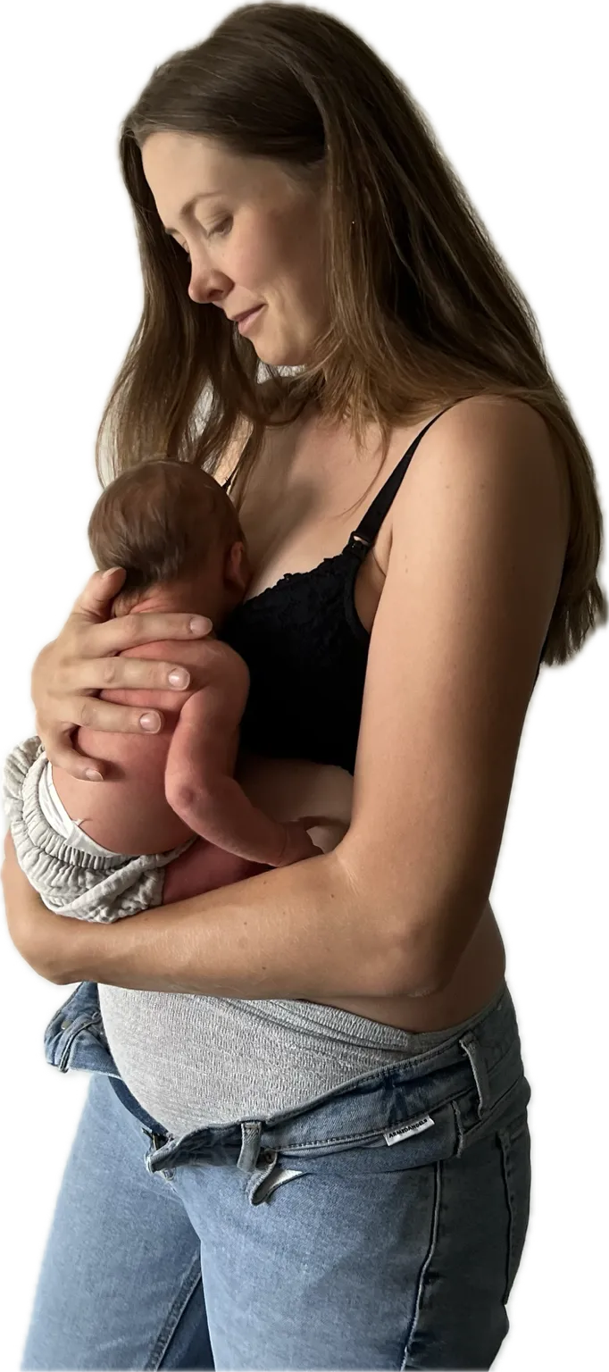 Laura hält ihr Neugeborenes eng an sich und schaut lächelnd auf das Baby hinunter.